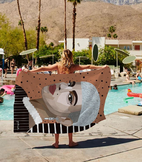 1. Woman holding Garbanota's Towel Roxy with artistic design by a poolside, showcasing unique hand-drawn artwork and vibrant colors