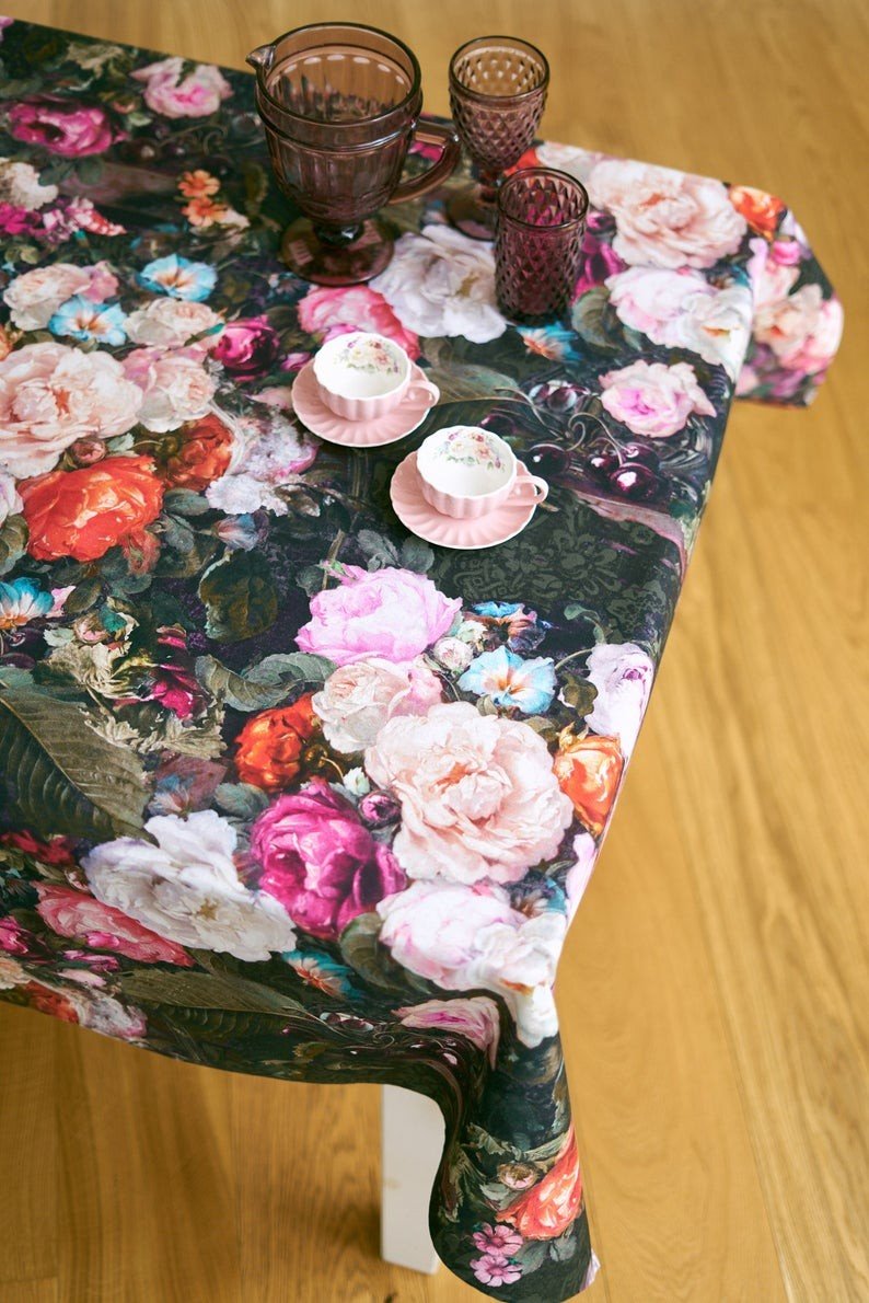 1. Dining table with Francine Black tablecloth featuring vibrant floral print, set with pink teacups and glassware, on wooden floor