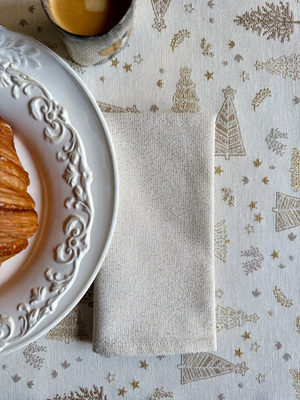 3. Close-up of Hortensias Home Golden Forest tablecloth showing intricate golden fir pattern with folded napkin and croissant