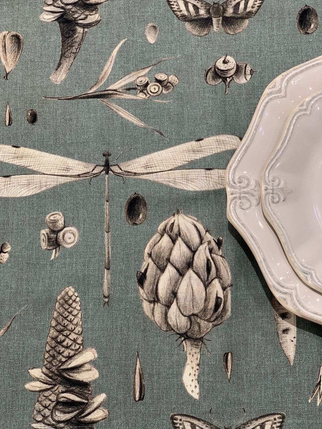 2. Close-up of aqua tablecloth with detailed botanical and insect print next to white ceramic plates