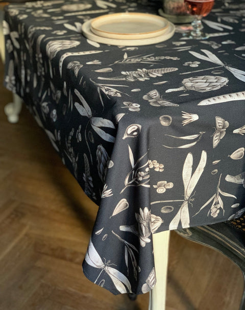 1. Rectangular tablecloth in Seeds Carbon print draped over dining table with plates and glass, showcasing elegant botanical design