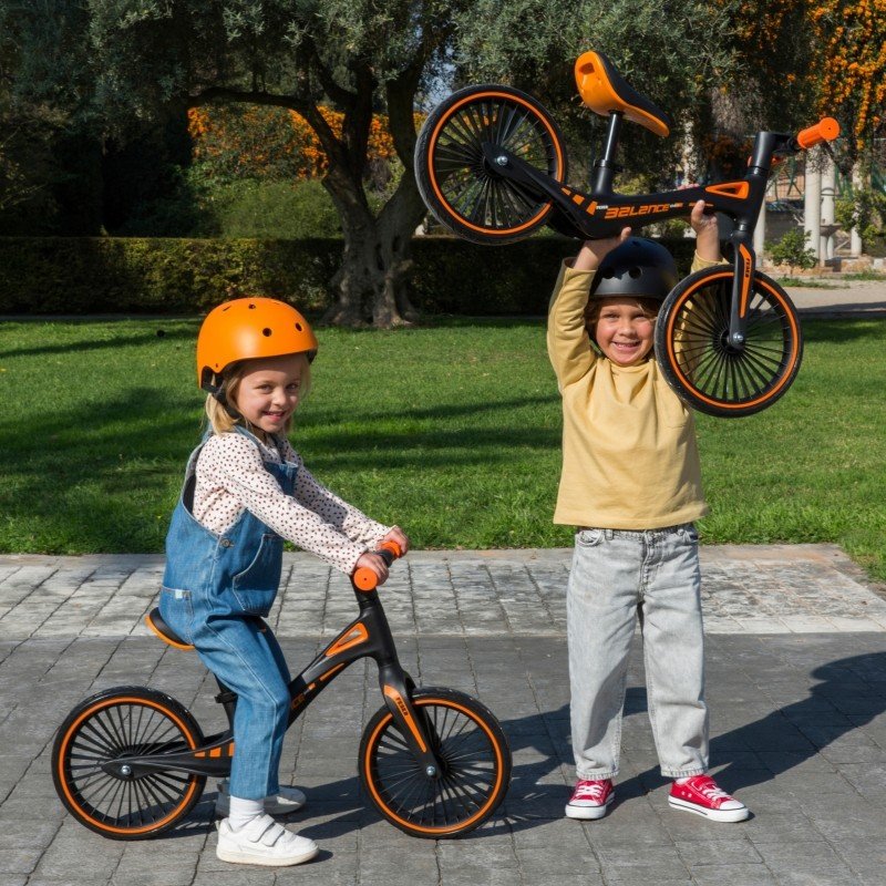 1. Two children with Feber balance bikes, one riding and one lifting bike in a park