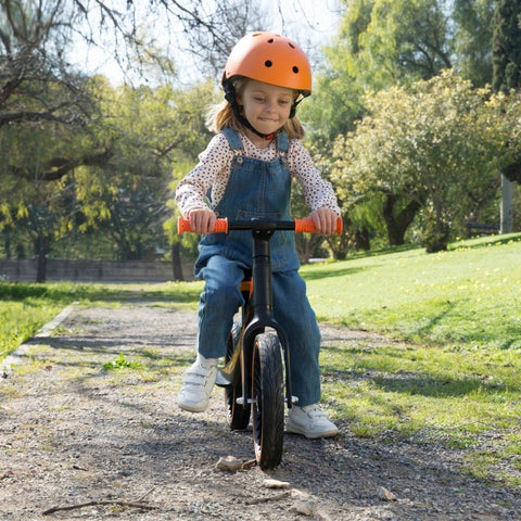 1. Girl wearing orange helmet riding Feber balance bike on a park path