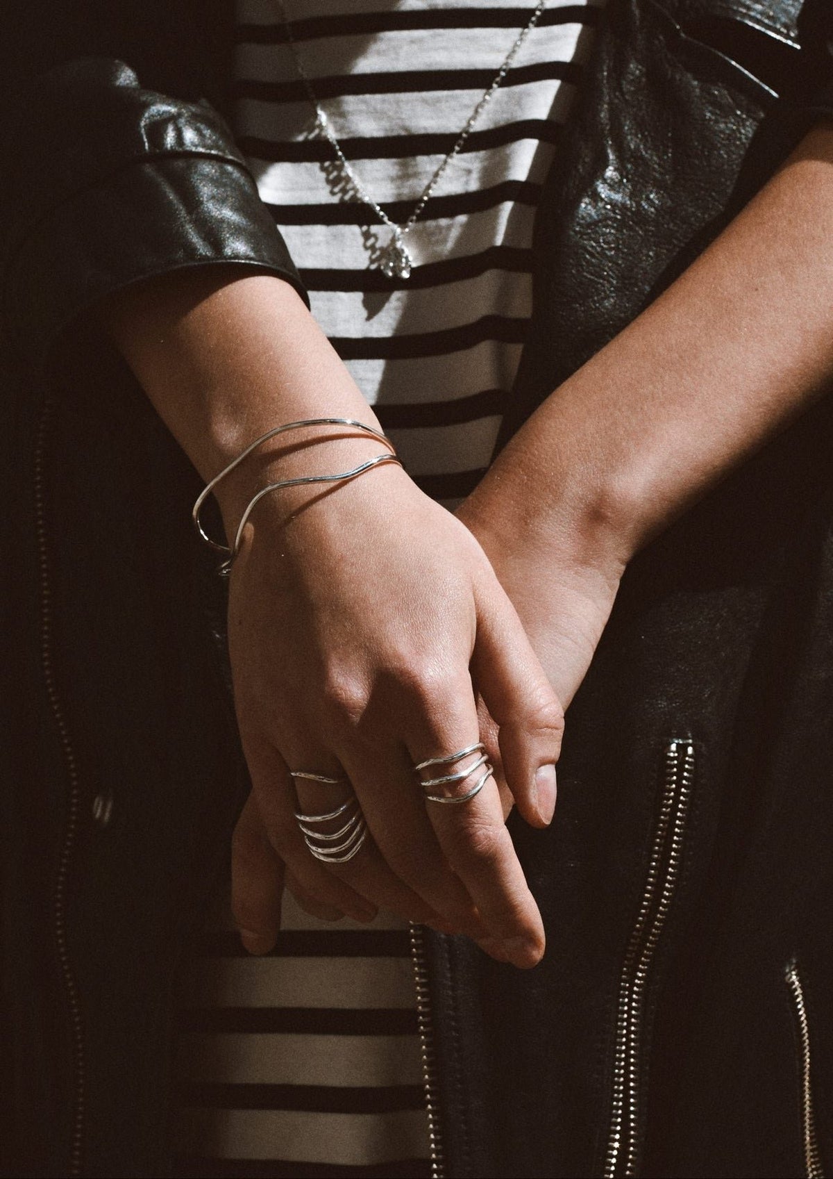 1. Women's hands adorned with NO MORE Reef Break Wave Ring in sterling silver, styled with a striped shirt and leather jacket