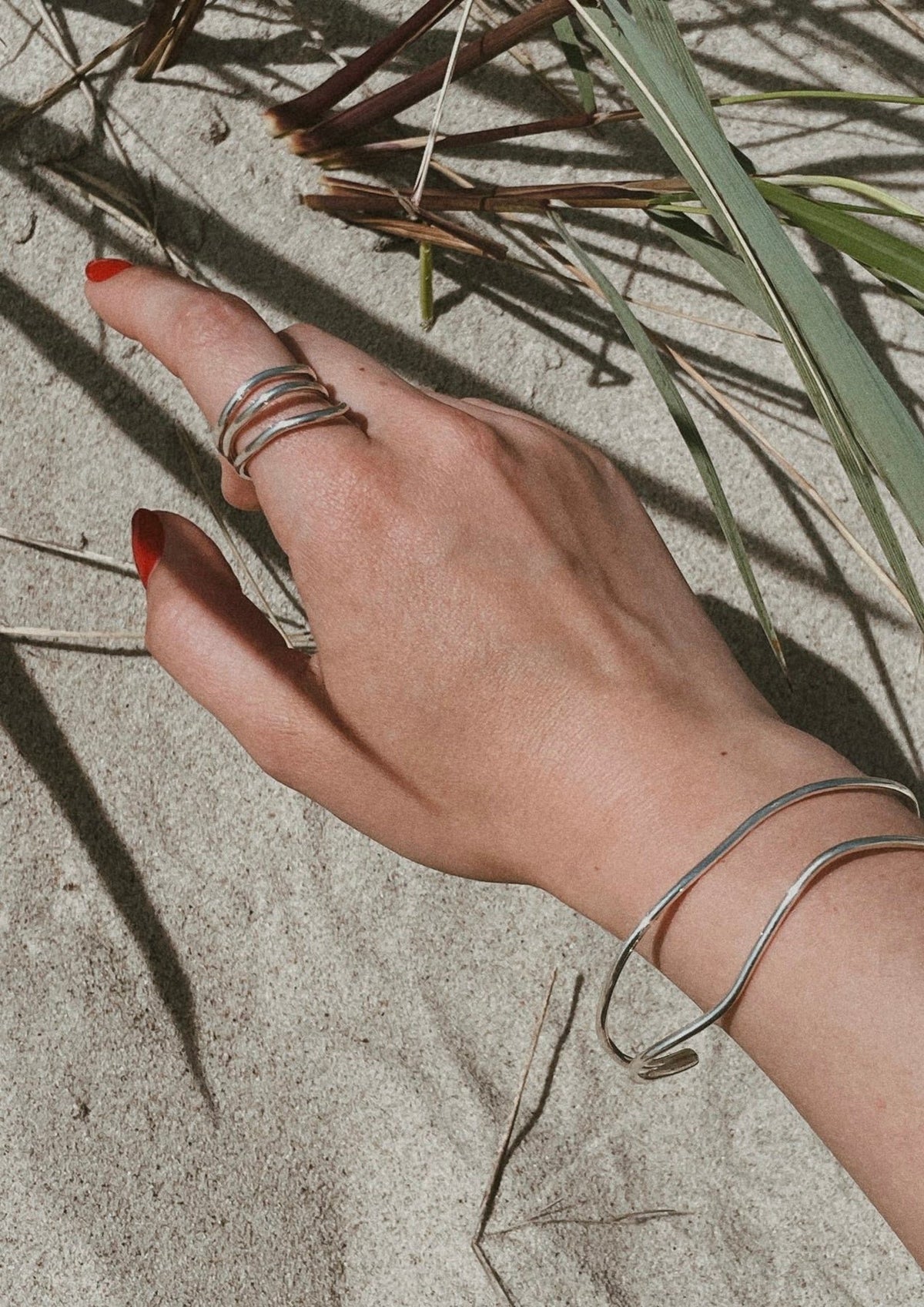 2. Close-up of woman's hand wearing NO MORE Reef Break Wave Ring in sterling silver on sandy beach