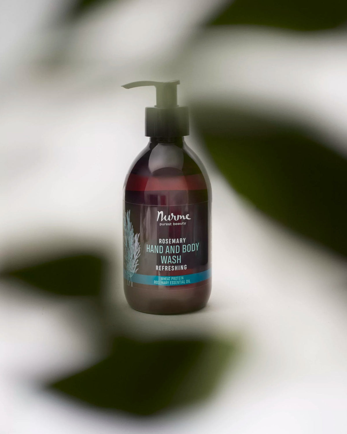 3. Nurme Refreshing Rosemary Hand and Body Wash 300 ml bottle with pump, partially obscured by green leaves, highlighting natural theme