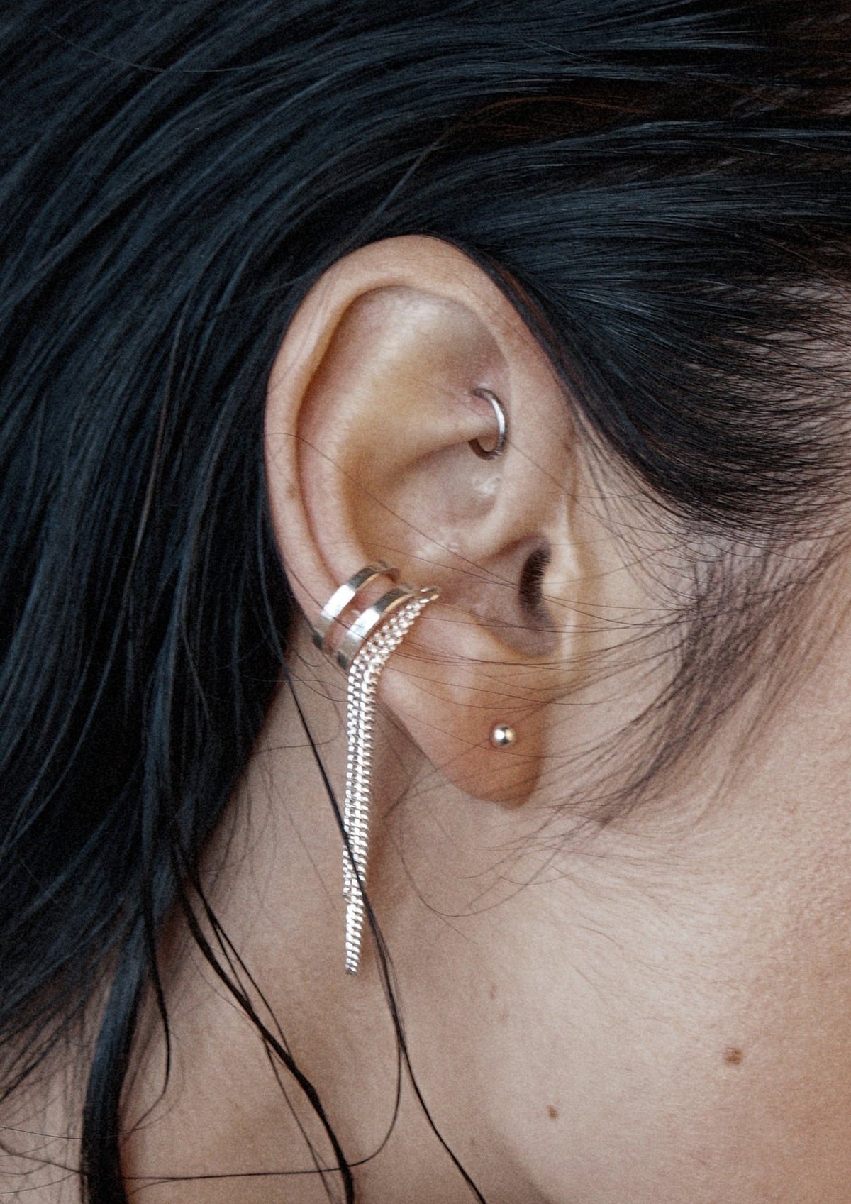 2. Close-up of NO MORE Revolve silver ear cuff with double chain on woman's ear