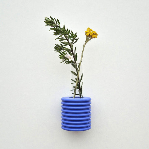 1. Ribble Wall Vase in blue by 5mm Paper, showcasing greenery and yellow flowers, studio setting