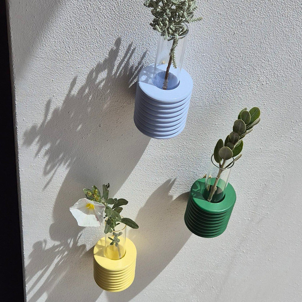 5. Close-up of Ribble Wall Vases in light blue, yellow, and green, with plants casting shadows