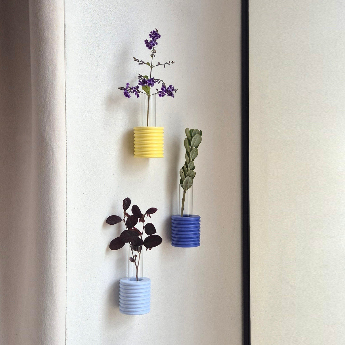 5. Trio of Ribble Wall Vases in blue, yellow, and light blue, displaying flowers on a wall