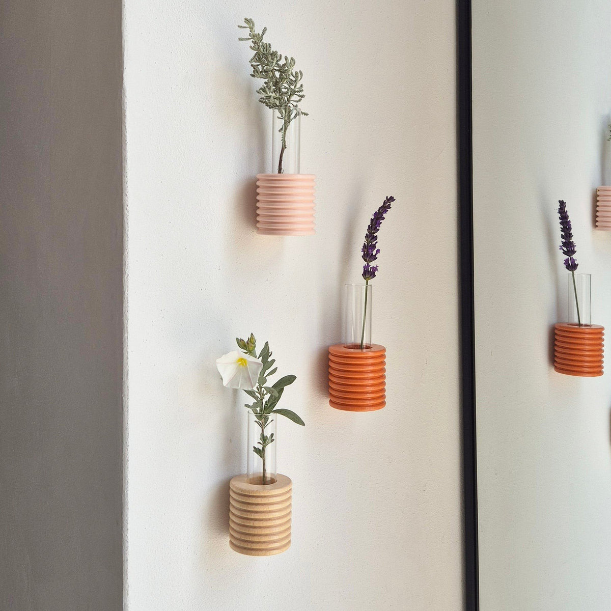 3. Lifestyle image of Ribble Wall Vases in orange and other colors, displayed with flowers on a wall