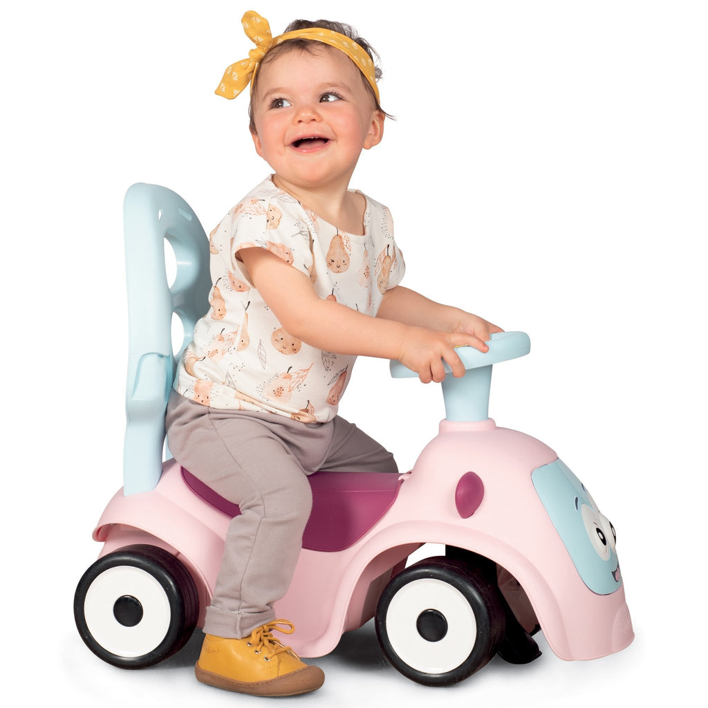 7. Child sitting on Smoby Ride-on Maestro 3in1 in pink, smiling and holding handlebars, wearing a yellow headband