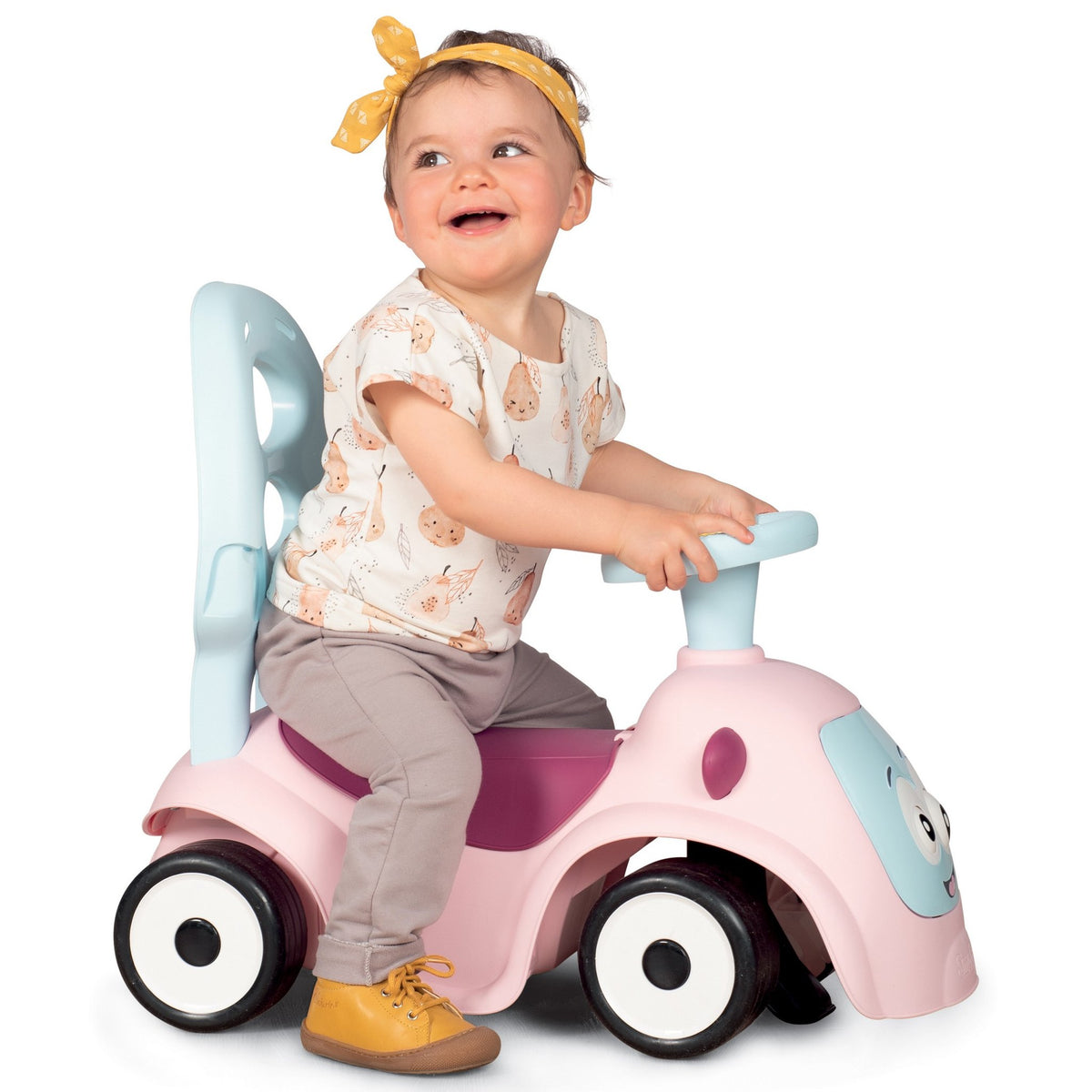 7. Child sitting on Smoby Ride-on Maestro 3in1 in pink, smiling and holding handlebars, wearing a yellow headband