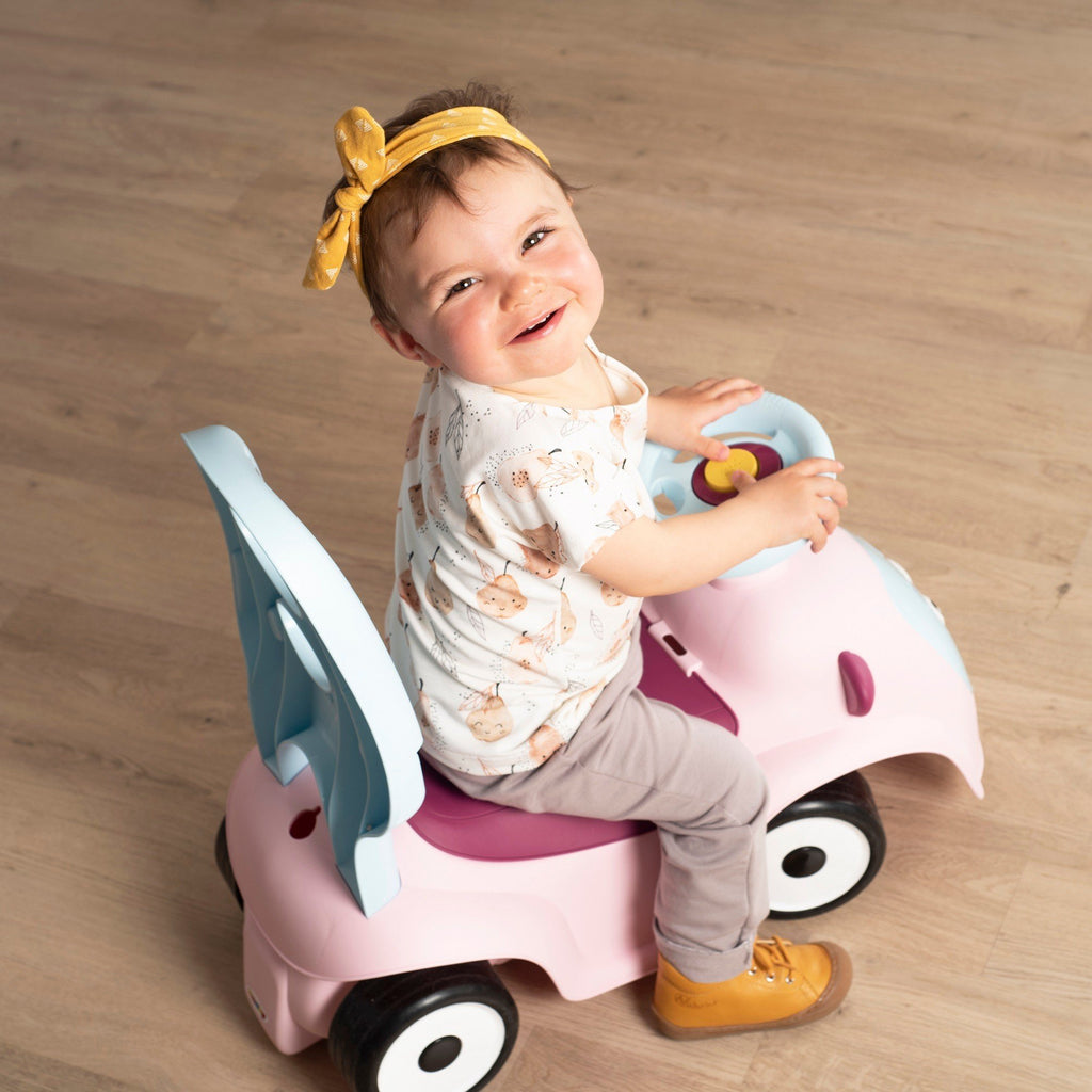9. Child riding Smoby Ride-on Maestro 3in1 in pink, smiling and looking up, wearing a yellow headband