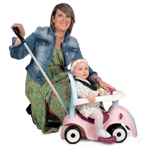 3. Woman pushing toddler on Smoby Ride-on Maestro 3in1 in pink, with safety ring and handle, in a studio setting
