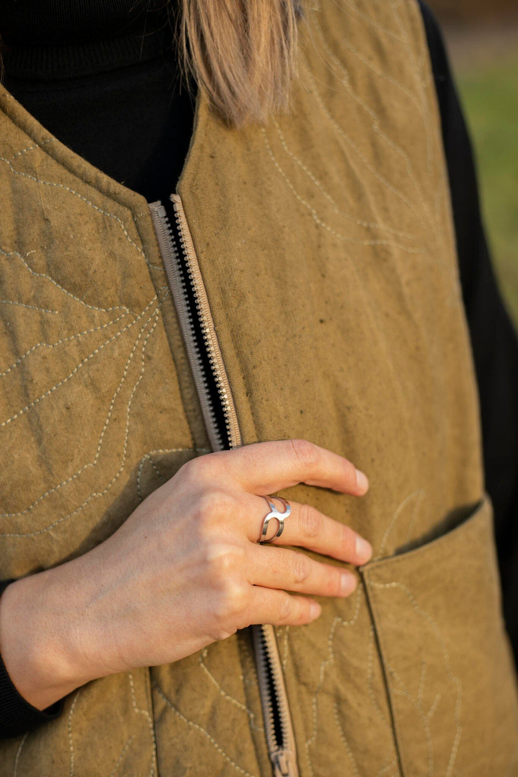 1. Woman wearing Lentsius stainless steel ring with open design, hand resting on brown quilted vest outdoors