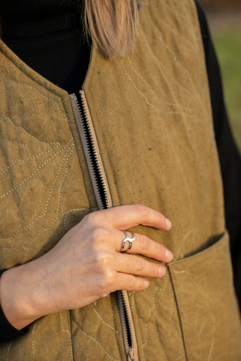 1. Woman wearing Lentsius stainless steel ring with open design, hand resting on brown quilted vest outdoors