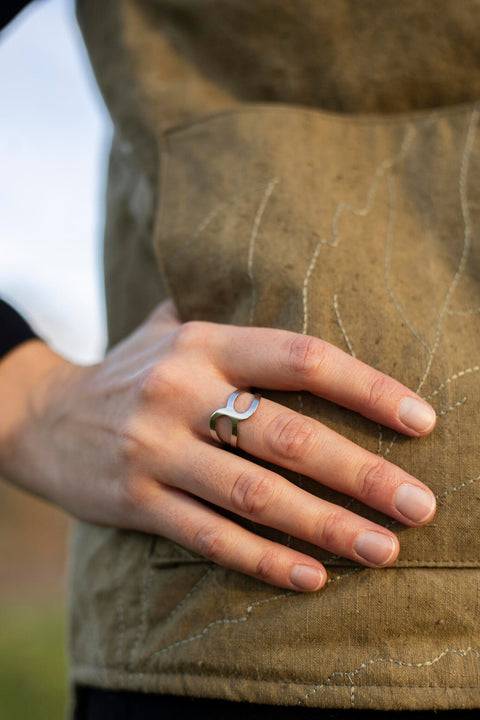 1. Close-up of woman's hand wearing Lentsius stainless steel ring with open design against brown quilted fabric