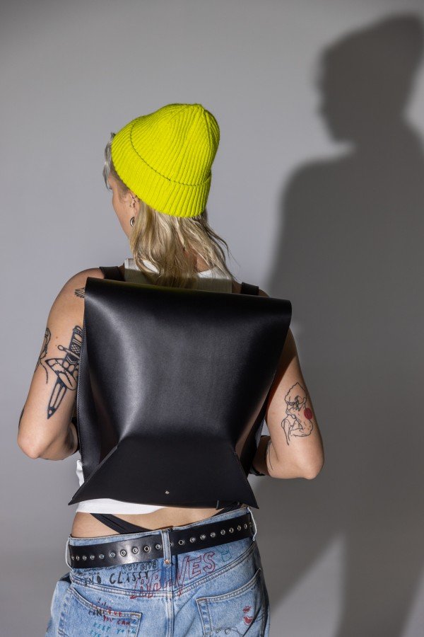 1. Woman wearing PYKOK Backpack Romeo in black leather, shown from the back with yellow beanie and tattoos, lifestyle setting