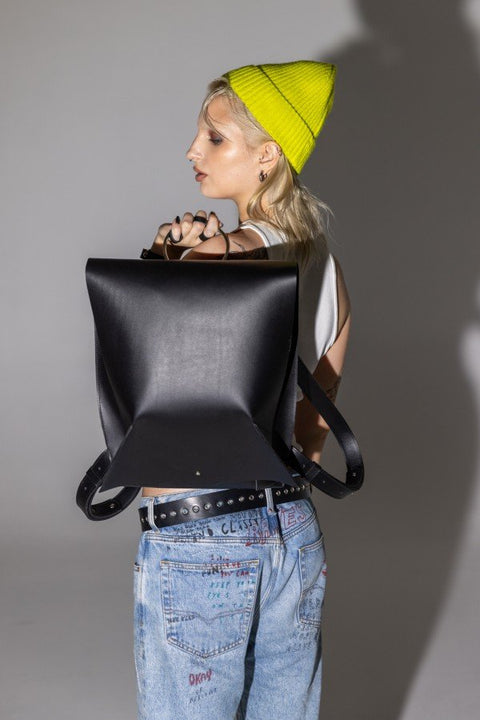 2. Woman holding PYKOK Backpack Romeo in black leather, side view with yellow beanie and casual outfit, lifestyle setting