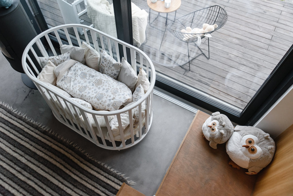 12. White round baby crib with bedding, placed near a window with a view