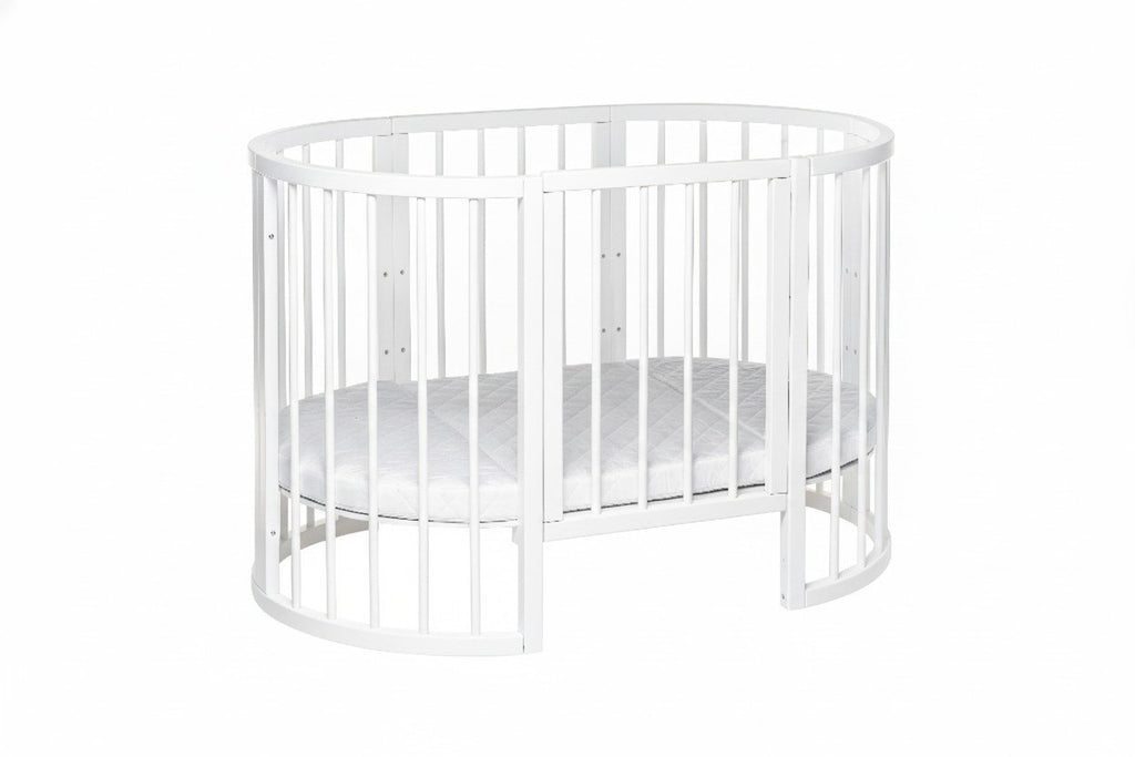 9. White round baby crib with mattress in studio setting, highlighting slatted design and removable side