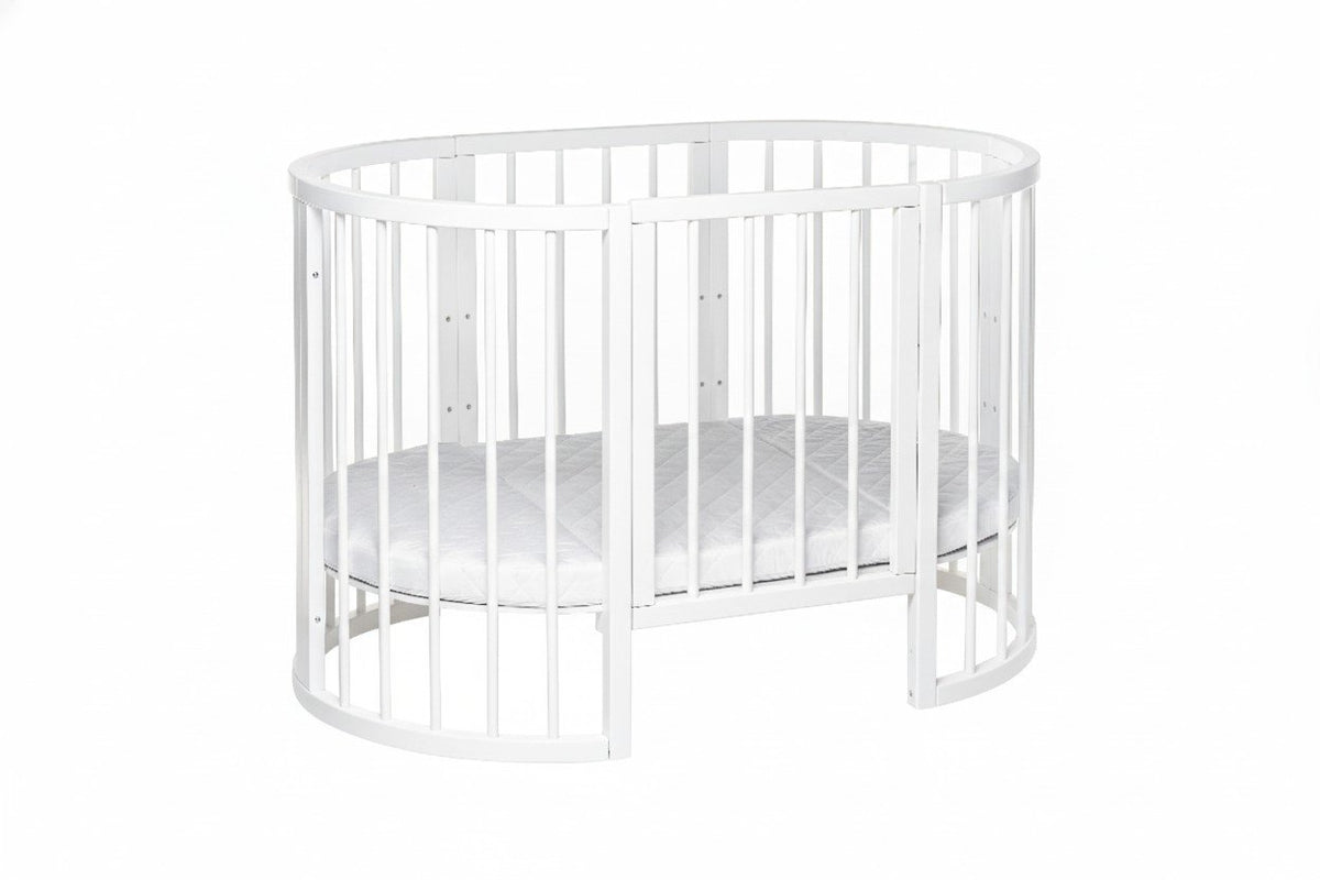 9. White round baby crib with mattress in studio setting, highlighting slatted design and removable side