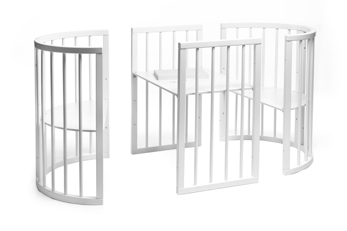 8. White round baby crib with adjustable base heights, shown in a studio