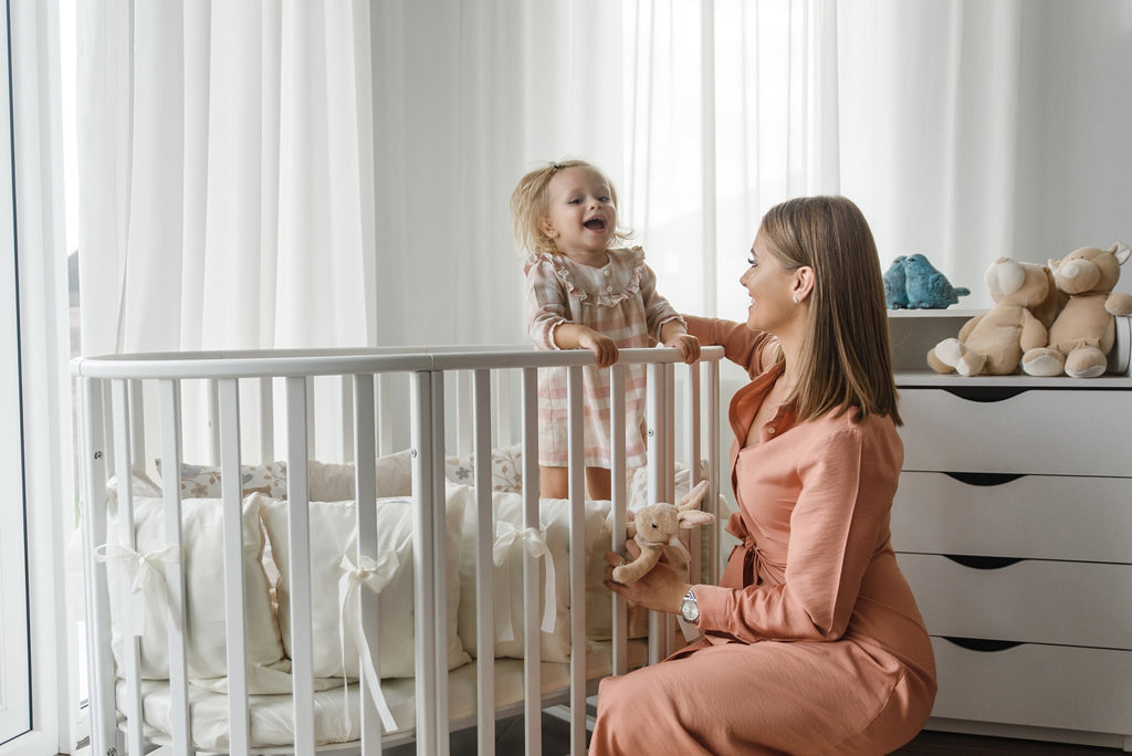 6. Woman interacting with child in white round crib, set in modern nursery with plush toys