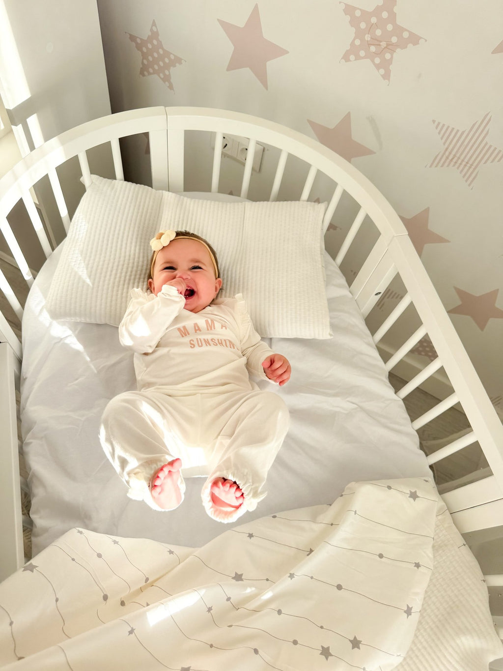 4. Baby lying in white round crib with star-patterned wall, showcasing cozy bedding