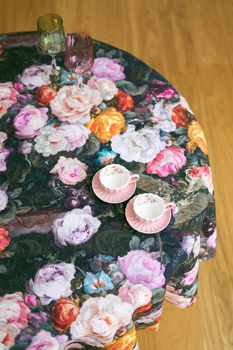 2. Overhead view of Francine black floral tablecloth with pink teacups and multicolored glasses on wooden table