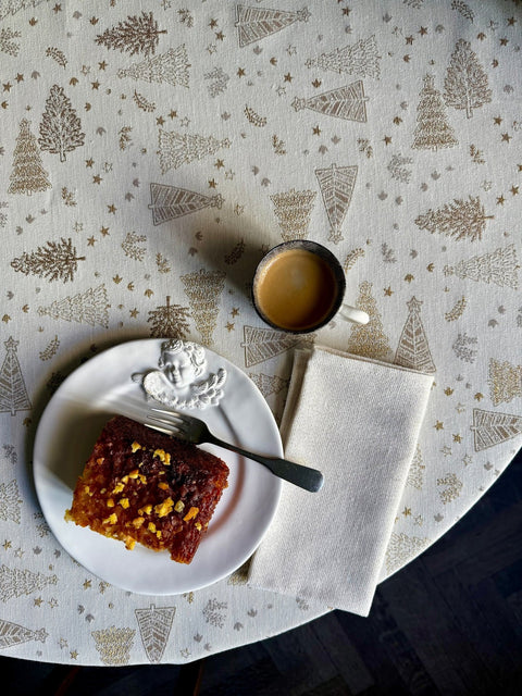 1. Round table with Golden Forest tablecloth featuring golden tree motifs, set with a slice of cake and coffee, creating a festive dining atmosphere