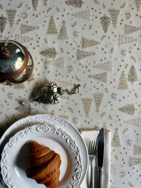 2. Round table with Golden Forest tablecloth displaying golden tree patterns, set with a croissant and decorative silverware, enhancing holiday dining decor