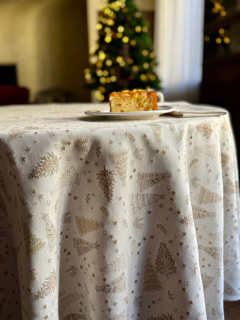 4. Round table with Golden Forest tablecloth in a holiday setting, featuring golden tree motifs and a slice of cake, creating a warm festive ambiance