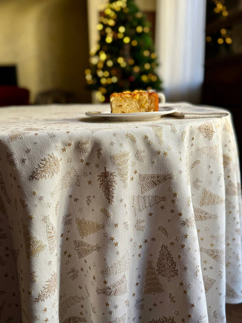4. Round table with Golden Forest tablecloth in a holiday setting, featuring golden tree motifs and a slice of cake, creating a warm festive ambiance