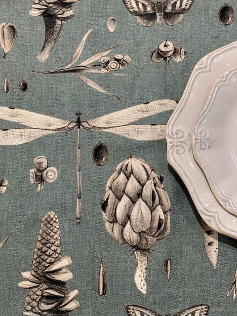 3. Detailed view of Seeds Aqua tablecloth with dragonfly and artichoke motifs next to white ceramic plates