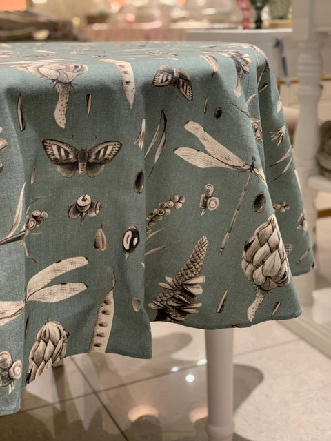 1. Round tablecloth in Seeds Aqua print draped over a table in a dining setting, showcasing intricate botanical and insect designs on 100% cotton fabric
