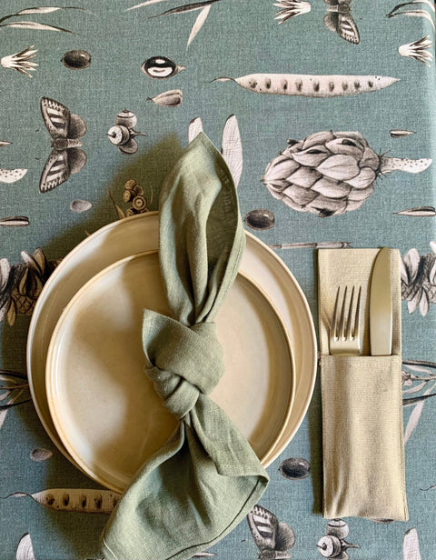 4. Flat lay of Seeds Aqua tablecloth with botanical print, featuring a place setting with green napkin and cutlery