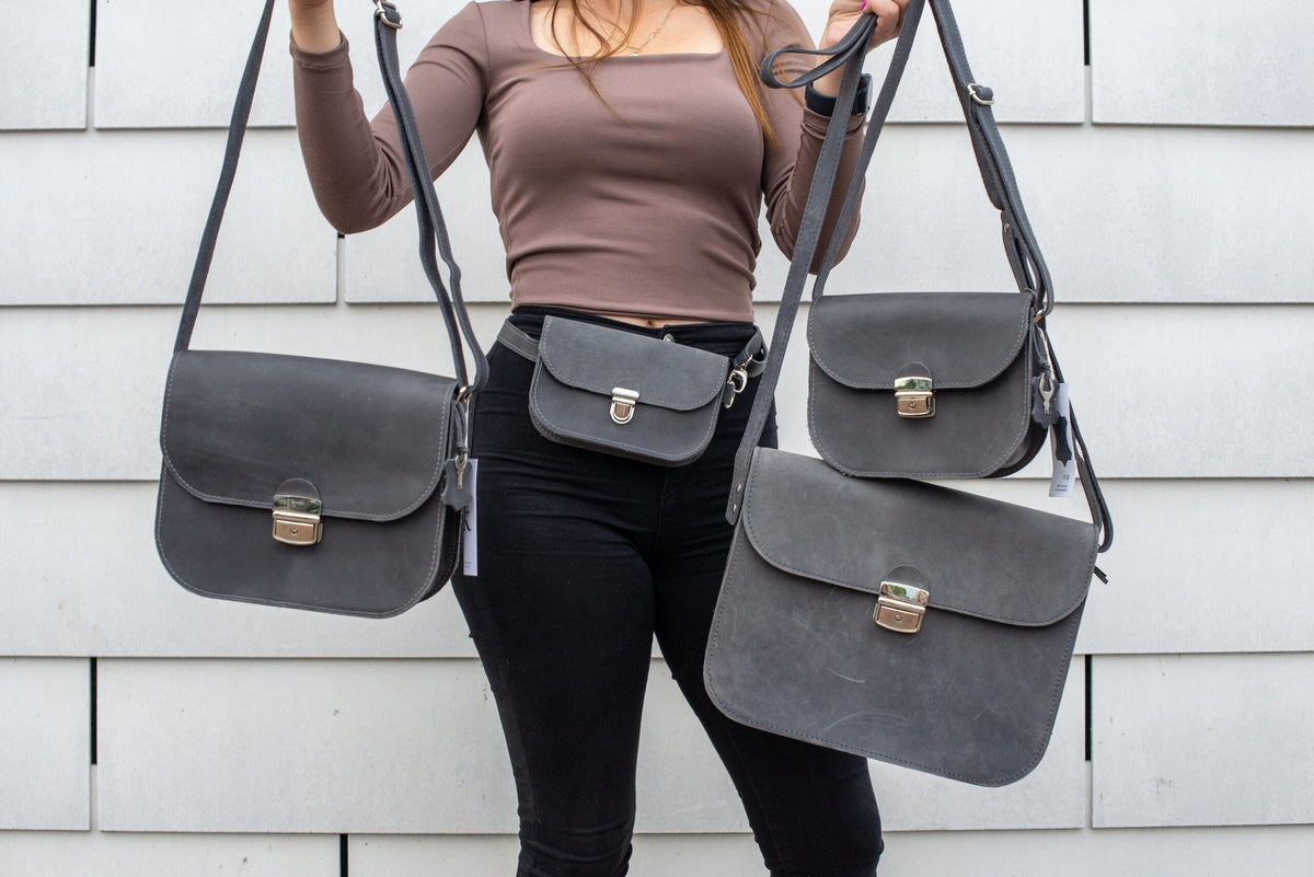 9. Woman holding multiple Zelma Kraft grey leather saddle bags, showcasing different sizes