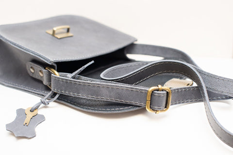5. Close-up of Zelma Kraft grey leather saddle bag showing adjustable strap and buckle closure