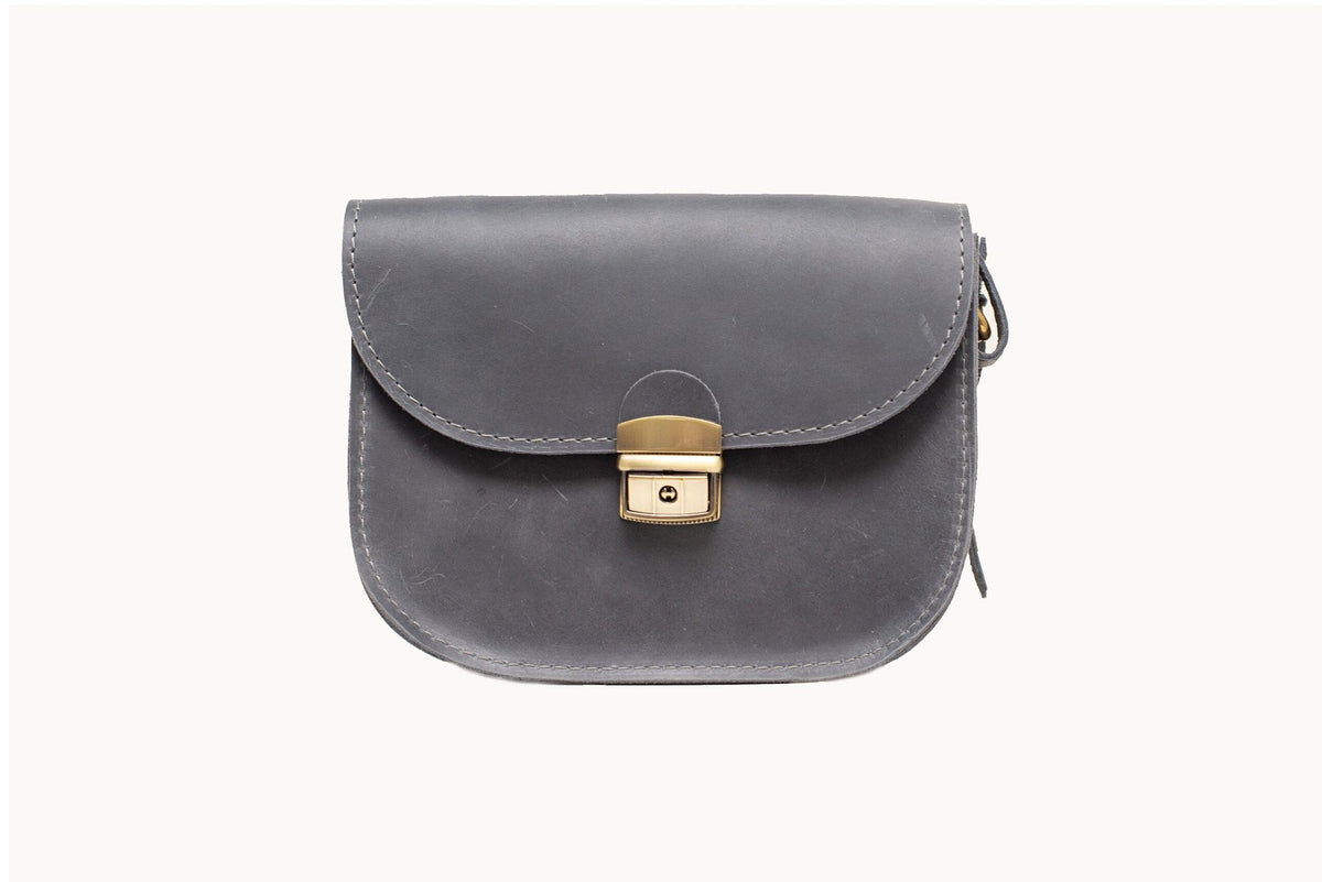 8. Studio image of the Zelma Kraft grey leather saddle bag with buckle closure, highlighting its sleek design
