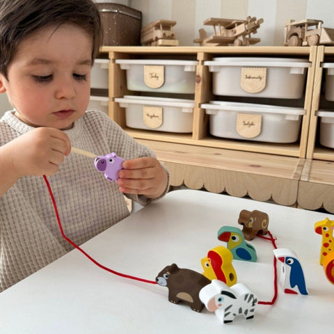 1. Child playing with Woopie Let's Go Green safari animal shaped wooden threading blocks at a table