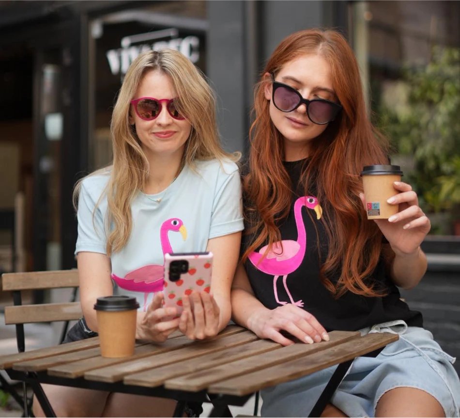 1. Women's Flamingo T-Shirt in light blue and black worn by two women at a cafe, showcasing casual style