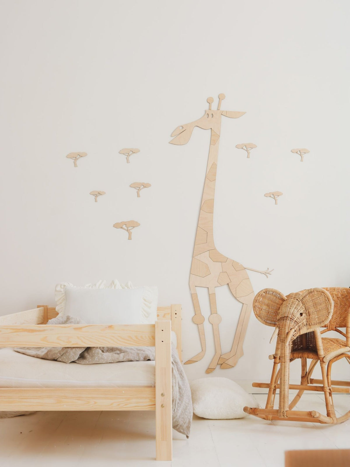2. Wooden giraffe wall decoration in child's room with wooden bed and wicker chair, small tree decals on white wall