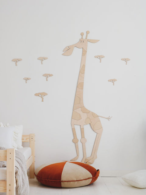 1. Wooden giraffe wall decoration in child's room with orange and white cushion and small tree decals on white wall