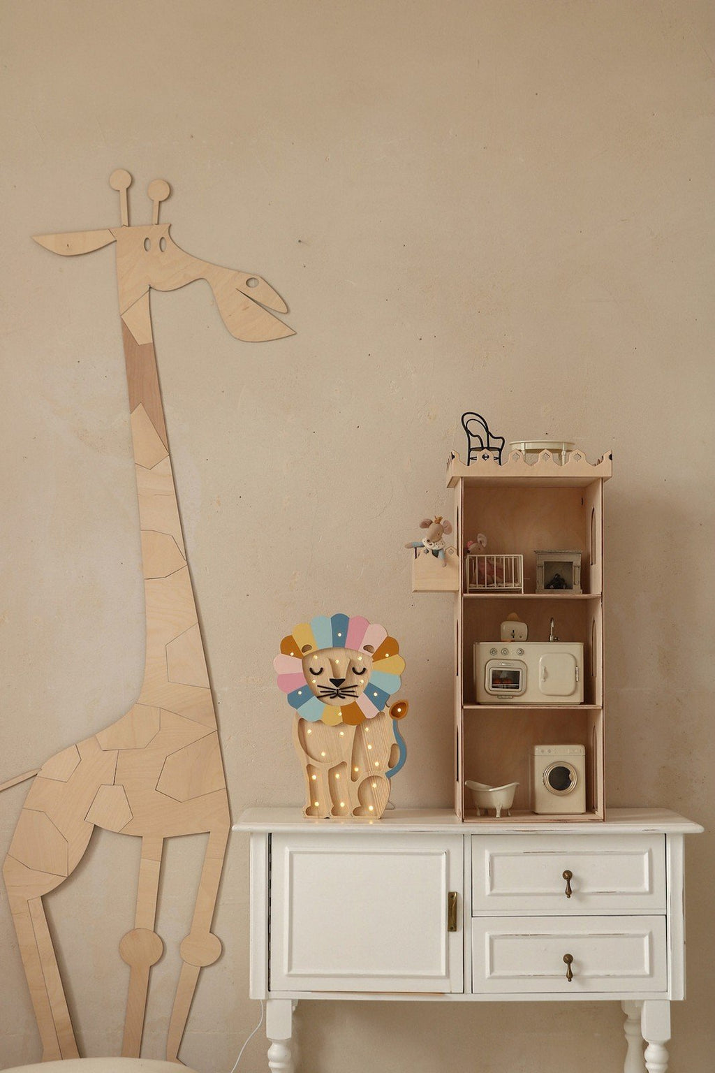 3. Wooden giraffe wall decoration next to white cabinet with colorful lion toy and small shelf in child's room