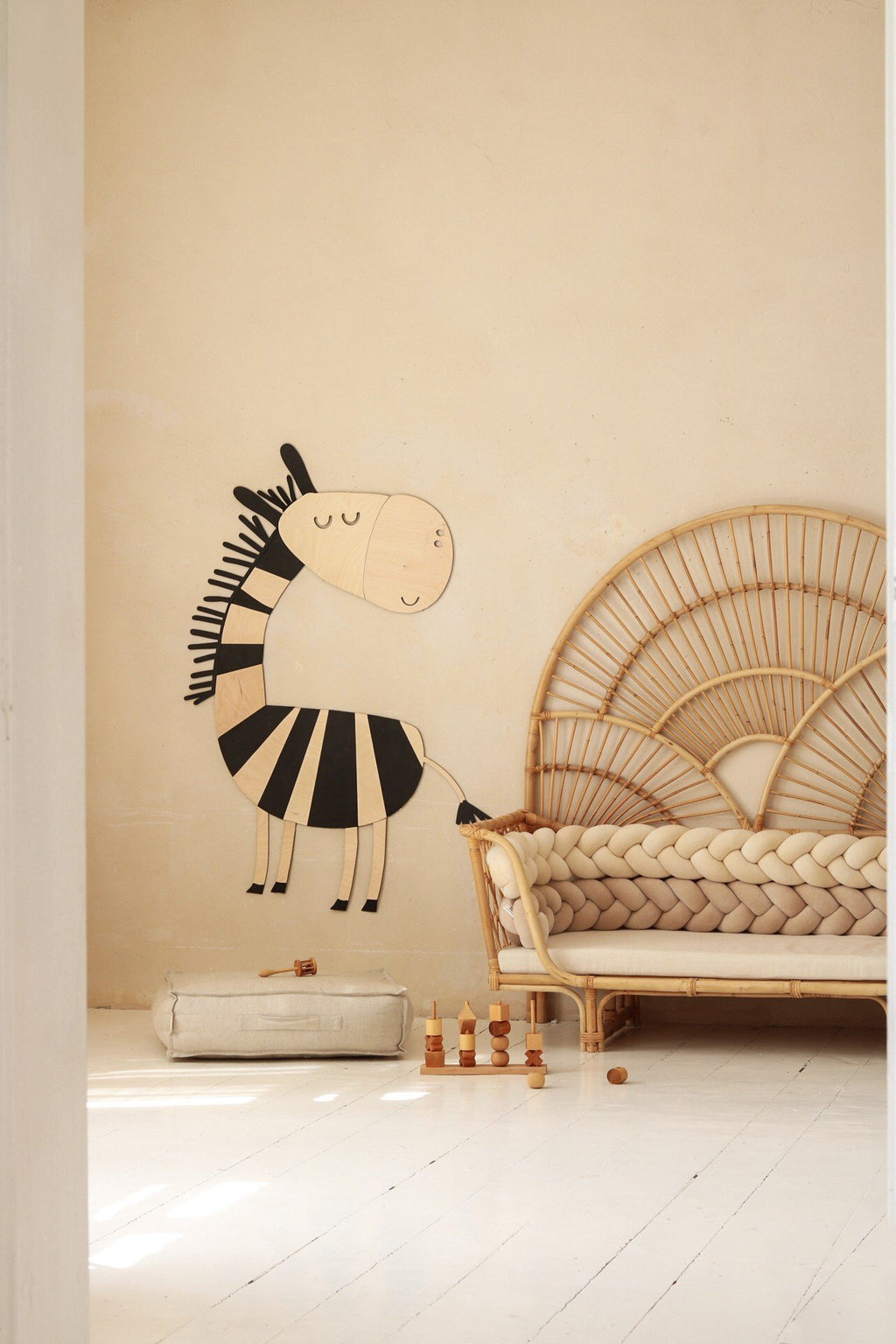 4. Wooden zebra wall decoration in a child's room with a rattan chair and braided cushion, soft toys on the floor