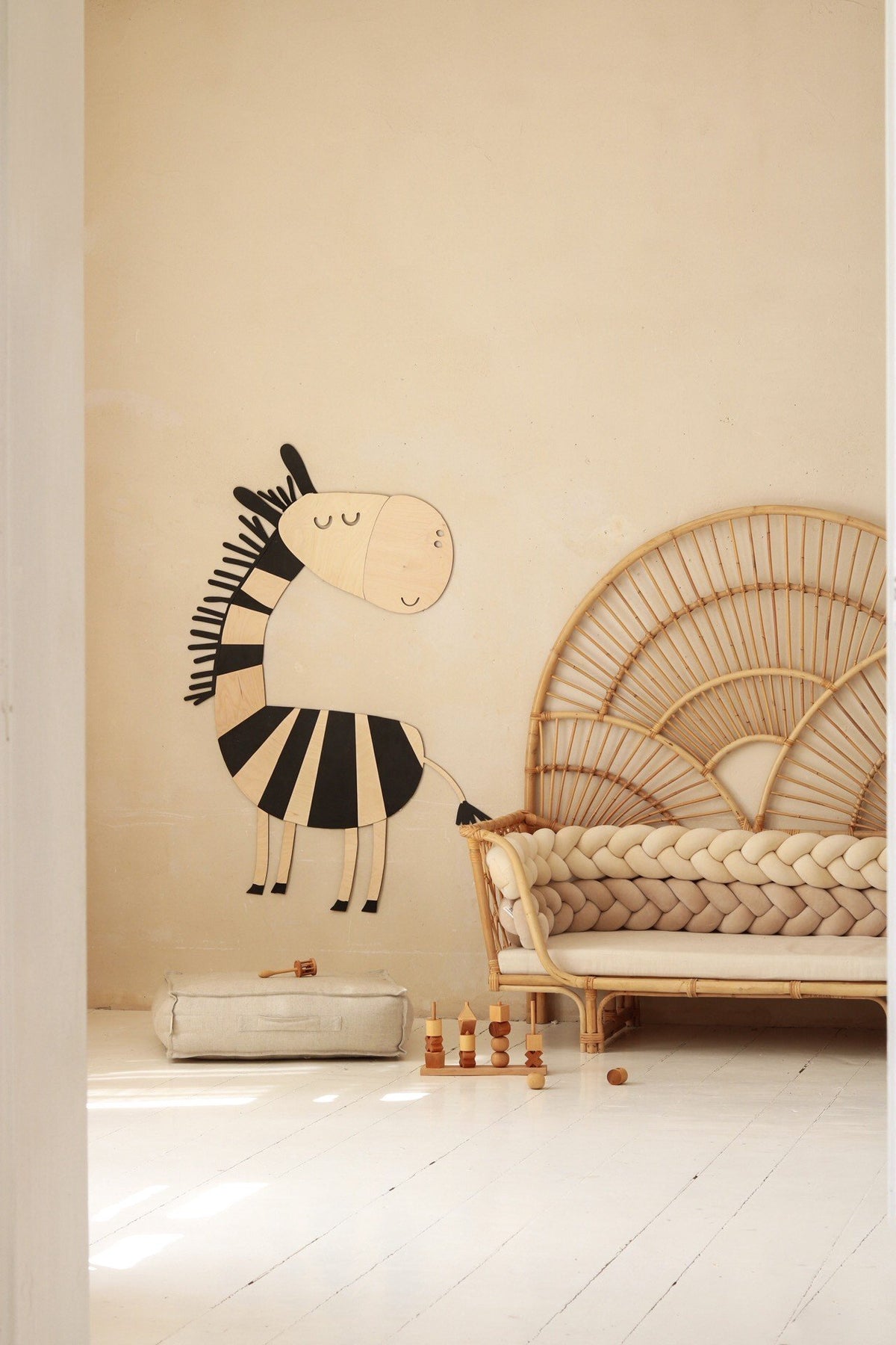 4. Wooden zebra wall decoration in a child's room with a rattan chair and braided cushion, soft toys on the floor