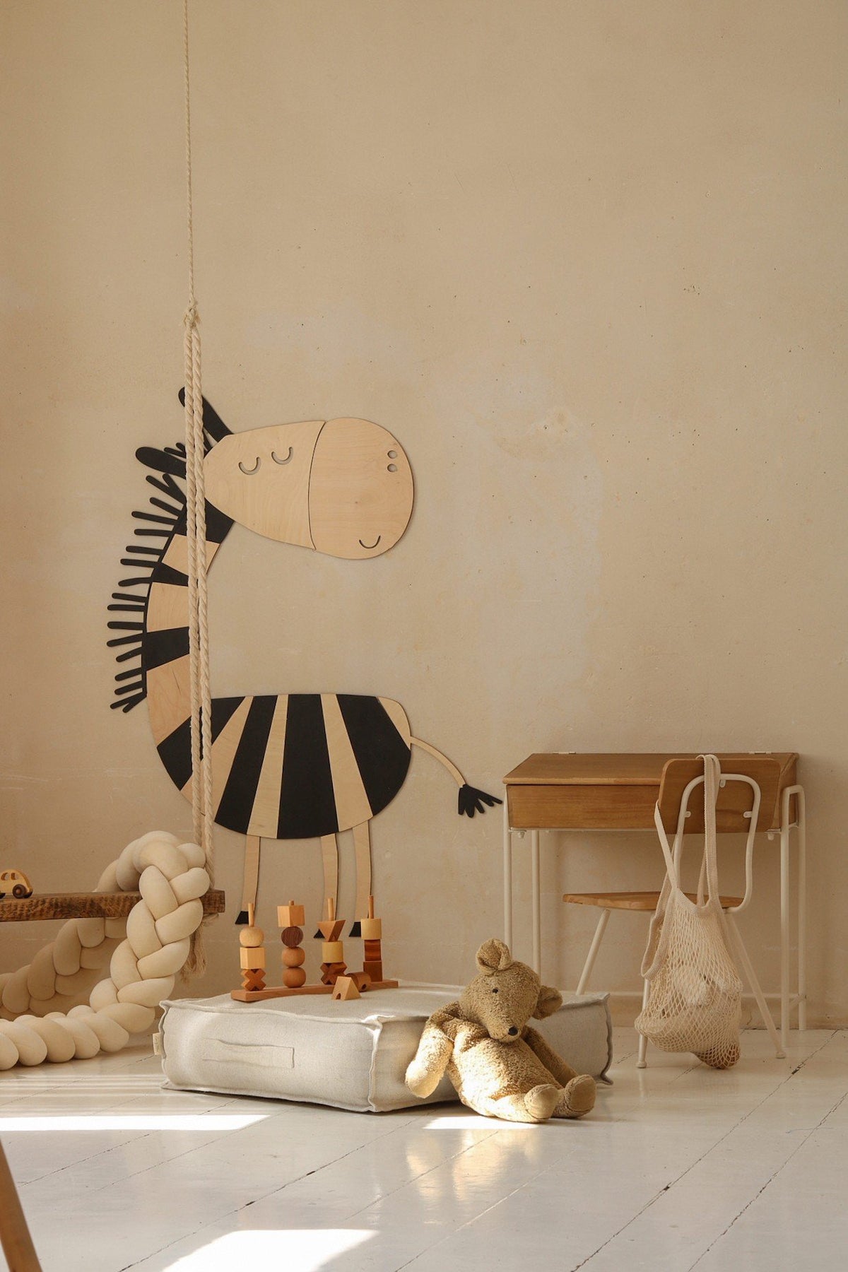 5. Wooden zebra wall decoration in a child's room with a small desk, chair, and plush toys on the floor