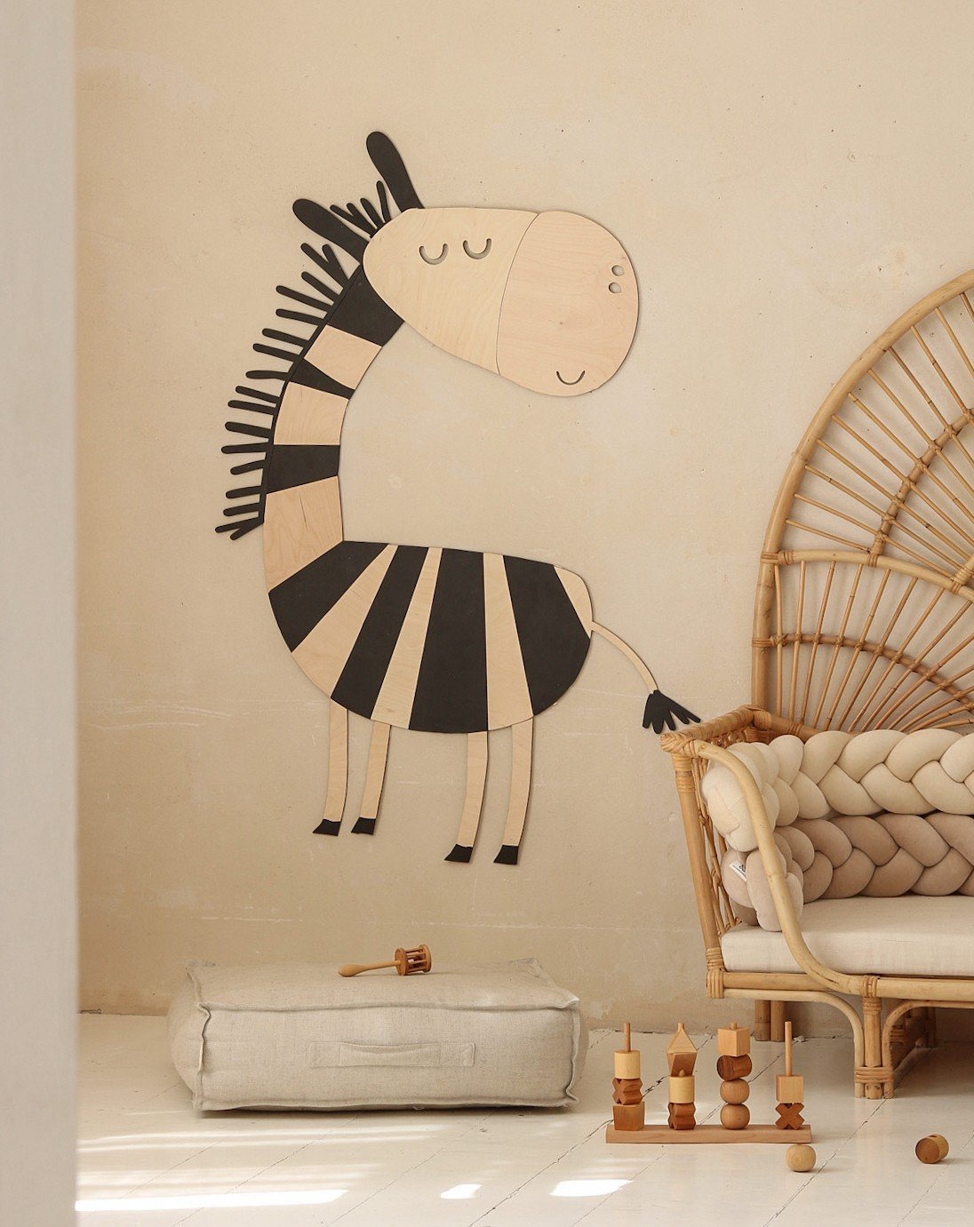 1. Wooden zebra wall decoration in a child's room with beige walls, next to a rattan chair and soft toys on the floor